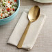 An American Metalcraft hammered gold vintage serving spoon on a napkin next to a bowl of rice.