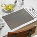 A table set with Front of the House Carbon Rush woven vinyl placemats, silverware, and glasses.