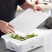 A person holding a white polyethylene food storage box lid over a container of lettuce.