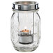 A Clear glass jar with a tealight candle inside.