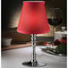 A Hollowick Empire Crimson candlestick shade on a silver stand with a red lamp.