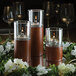 Three Hollowick wood cylinder candle holders on a table with lit candles.