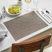 A table with a Front of the House Copper Basketweave placemat and a plate of salad with silverware and glasses of wine.