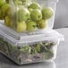 Two Vigor clear polycarbonate food storage containers on a counter filled with green apples and greens.