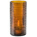 A dark amber glass cylinder with a wavy design holding a candle