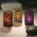 Three Hollowick crackle blue and purple glass cylinder lamps with lit candles on a table.