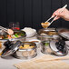 A hand holding Town stainless steel dim sum steamer covers over a variety of food containers.