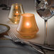A Hollowick satin gold glass votive candle holder with a lit candle inside.