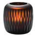 A black Hollowick glass votive holder with a wavy pattern, holding an orange candle.