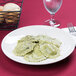 A Tuxton Venice ivory china plate with a plate of ravioli and a glass of water on a table.