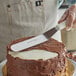 A person using a Dexter-Russell offset icing spatula to spread chocolate on a cake.