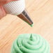 A person using an Ateco plain piping tip to frost a cupcake with green frosting.