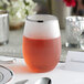 A close-up of a Visions plastic stemless wine glass with a silver rim filled with red liquid on a table.