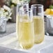 Two Visions clear plastic stemless champagne flutes with silver rims filled with yellow liquid.