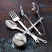 Oneida Cooper stainless steel serving tongs on a table with spoons and forks.