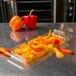 A Carlisle amber plastic food pan with sliced red, yellow, and orange peppers on a table.