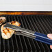 A person using Vollrath VersaGrip tongs with a blue Kool Touch handle to hold meat over a grill.