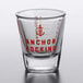 An Anchor Hocking shot glass with red print and graduations.