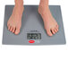 A person standing on a Cardinal Detecto SlimTALK low-profile digital scale with their feet on it.