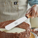 An Ateco straight spatula with a wood handle being used to cut a frosted cake.