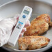 A person using a Comark digital infrared thermometer to measure the temperature of meat.