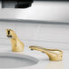 A close-up of a Bobrick polished brass counter-mounted automatic faucet above a sink.