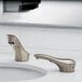 A bathroom sink with two Bobrick brushed nickel counter-mounted automatic soap dispensers and faucets above.