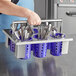 A person holding a metal rack with purple Steril-Sil plastic containers of silverware.