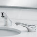 A Bobrick polished chrome counter-mounted automatic faucet over a white sink in a bathroom.