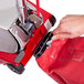 A hand using a Sanitaire upright vacuum to remove a metal hook from a red bag.