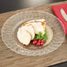 A Fineline clear plastic plate with sliced turkey and vegetables on it.