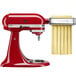 A white KitchenAid pasta cutter attachment set on a red KitchenAid mixer.