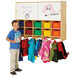A boy standing next to a Jonti-Craft wall mount coat locker with colored trays.