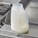 A plastic jug of milk sitting inside a Tablecraft 32 oz. dispenser jar with a handle.