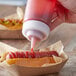 A hand using a Tablecraft Wide Tip Cap to pour pink sauce onto a hot dog.