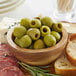 A wooden cutting board with a bowl of Frutto d'Italia Pitted Green Castelvetrano Olives and bread.
