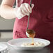 A person using a Vollrath stainless steel ladle to pour syrup over a white plate.