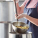 A woman in a blue apron using a Vollrath stainless steel ladle to serve food.