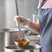 A person using a Vollrath stainless steel ladle to serve soup from a pot.