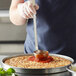 A person using a Vollrath stainless steel ladle to put food on a pizza.