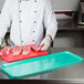A chef cutting meat on a green Cambro market tray.