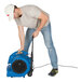 A man using an XPOWER blue air mover with wheels and a telescopic handle to clean a floor.