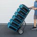 A man pushing a hand truck with several blue XPOWER air movers.