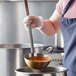A person using a Vollrath stainless steel ladle to serve red sauce.
