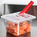 A clear plastic Cambro food pan lid with a spoon notch holding tomatoes with a red spoon.