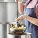 A woman in a blue apron using a Vollrath stainless steel ladle to serve food from a pot.
