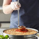 A person using a Vollrath stainless steel ladle to put sauce on a pizza.