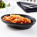 A Tuxton black oval china baker filled with pasta and a bowl of salad on a table.
