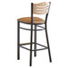 A Lancaster Table & Seating black bistro bar stool with a light brown cushion and natural wood back.