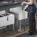 A woman standing at a Regency stainless steel underbar drainboard next to a counter with a glass.
